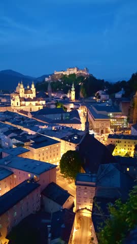 Vertical perspective of the historic city center of Salzburg at night, highlighting the illuminated Cathedral and Hohensalzburg Fortress.