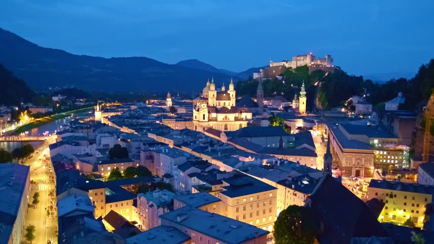 A horizontal video panning across the illuminated skyline of Salzburg, Austria, at night, featuring the fortress, cathedral, and Salzach river.