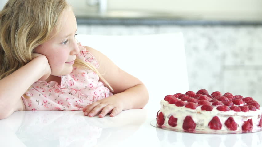 Little girl sitting at table and admires cake
