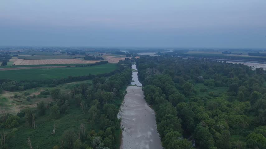 Po River low water reveals a broad exposed channel between riparian woodland and cultivated fields in Piacenza province, Emilia Romagna, Po Valley, Italy, drone tilt down reveal.