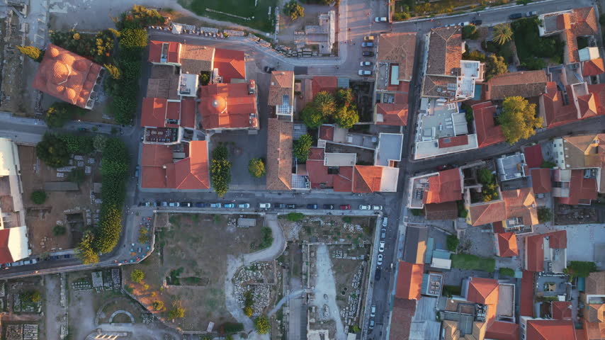 Top-down aerial rotating perspective of the Roman Agora ruins and the historic Plaka district, showcasing the ancient archaeological site surrounded by the modern city of Athens at sunset