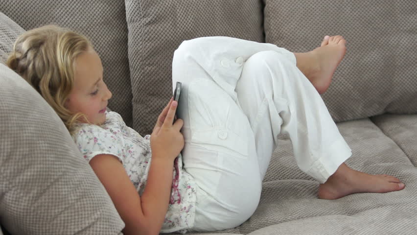 Little girl with phone lying on a sofa
