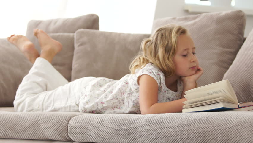 Sweet girl resting on the couch and reading a book
