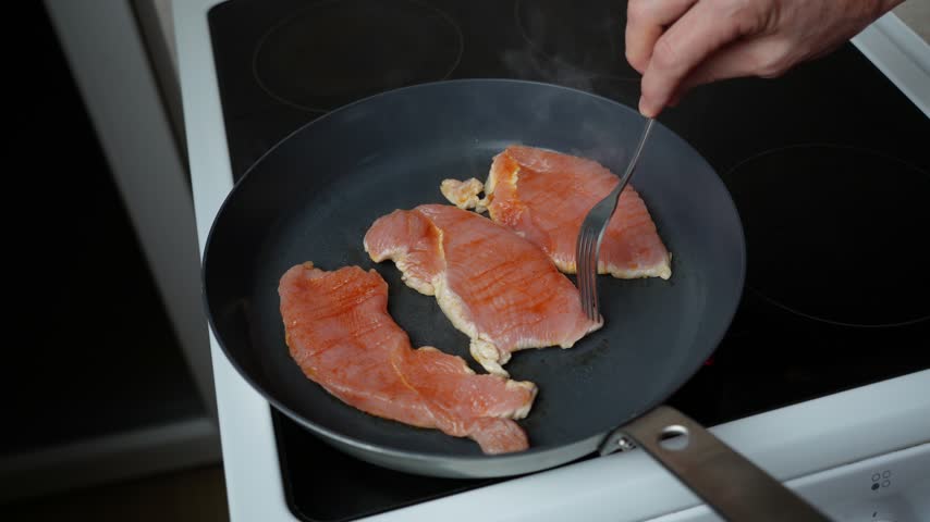 Turning Turkey Steak Over in a Frying Pan. A turkey steak is turned over with a fork in a hot frying pan while cooking to brown both sides evenly.