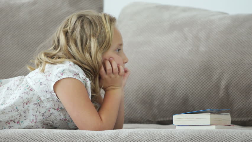 Little girl lying on sofa and reading book
