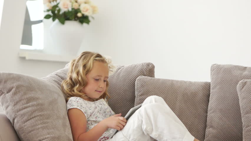 Little girl sitting on sofa with tablet pc
