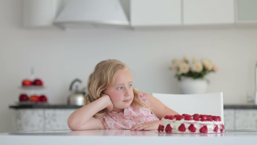 Little girl thinks about something and looks at a strawberry cake
