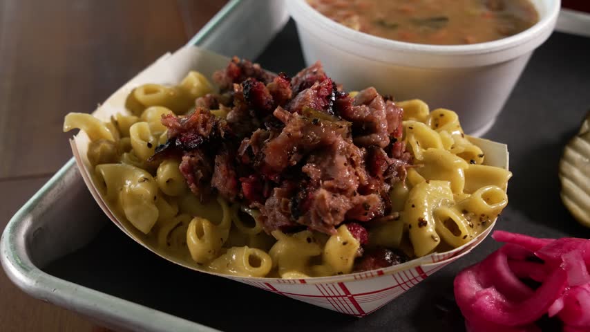 Creamy hatch macaroni and cheese topped with smoky chopped barbecue brisket, served alongside pinto beans and pickled onions, close up, slider, 4K