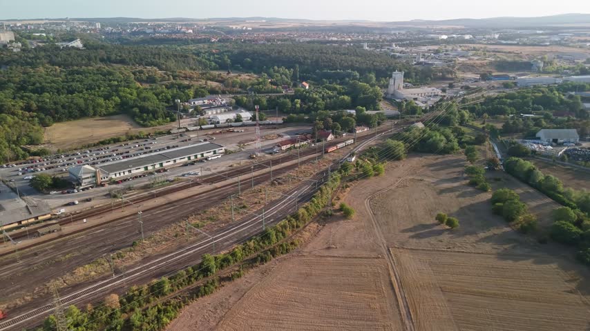 Veszprém, Hungary railway station and rail yard with passenger and freight trains, tracks, warehouses and residential areas in an urban transport hub, viewed by drone.