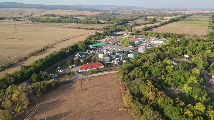 Veszprém, Hungary sewage treatment plant with water tanks, clarifiers and service roads amid rural fields and trees in summer daylight, viewed from an aerial perspective.