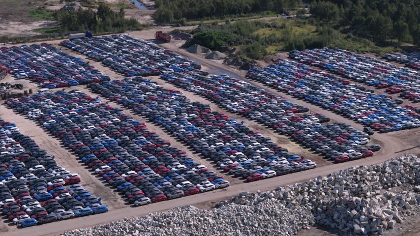 An aerial view showing a sprawling outdoor storage lot filled with rows of new passenger vehicles, highlighting automotive manufacturing distribution