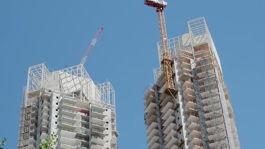 Low angle view of two high rise residential towers under construction with cranes against a clear blue sky in Tel Aviv, Israel, showcasing modern urban development and real estate growth