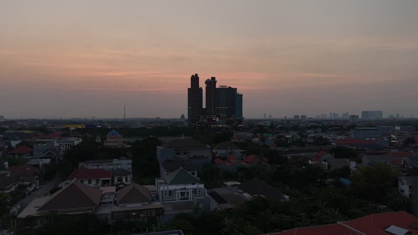 Aerial drone view of Surabaya cityscape at sunset with dramatic orange sky, high-rise apartment towers and dense residential neighborhoods in East Java, Indonesia