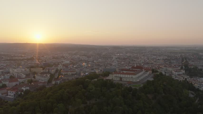 Špilberk Castle crowns a wooded hill as the sun rises over the wide urban landscape of Brno.