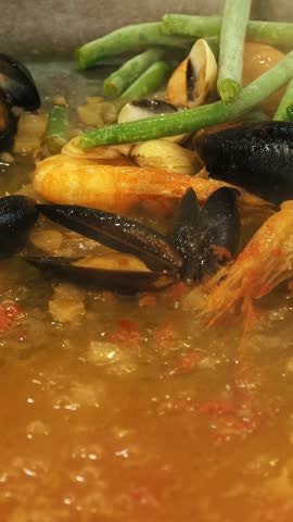 Cooking seafood. close-up. frying mussels and shrimp with green peas, string beans, garlic, spices and tomato sauce in a large wok .
