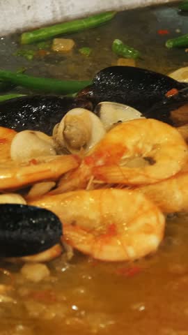 Cooking seafood. close-up. frying mussels and shrimp with green peas, string beans, garlic, spices and tomato sauce in a large wok .