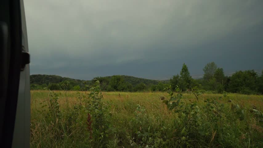 Lightning flash strike across dark storm clouds over green grassy field viewed from open camper van door