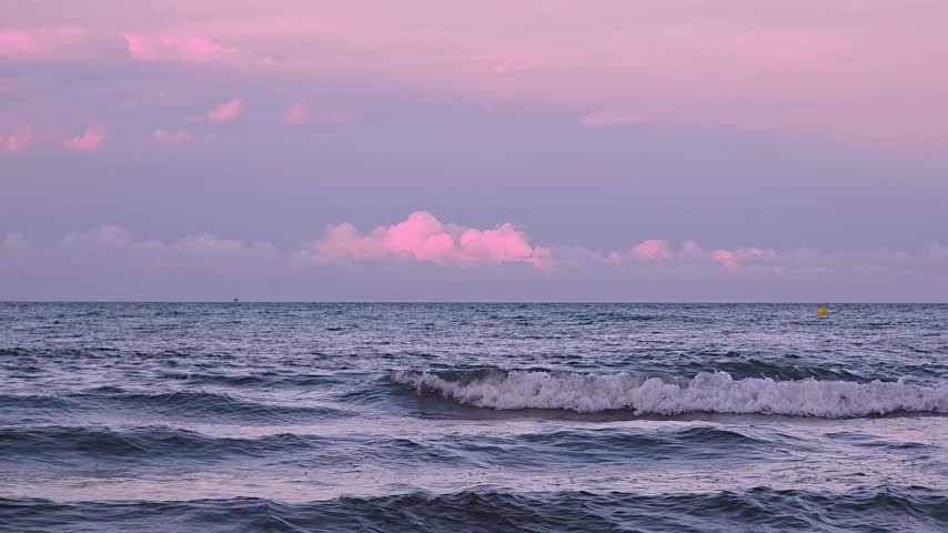Dramatic purple sunset over sea waves with fluffy cumulus clouds on horizon during twilight.