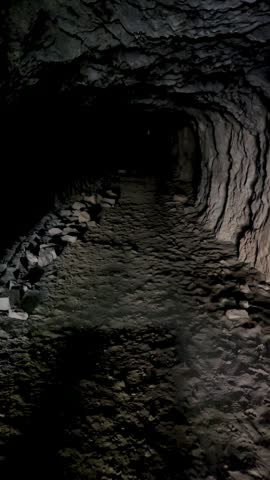 First-person perspective walking inside a pitch-black cave tunnel with narrow light opening ahead.