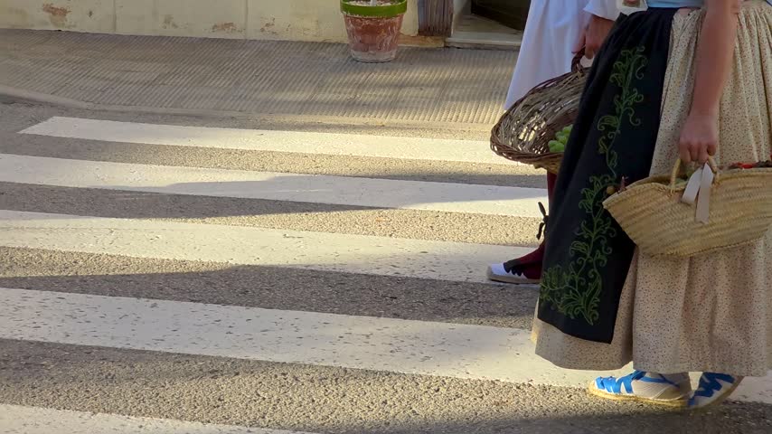 People in traditional Valencian costumes walking with woven baskets of freshly harvested grapes during a local festival in Teulada, Spain.