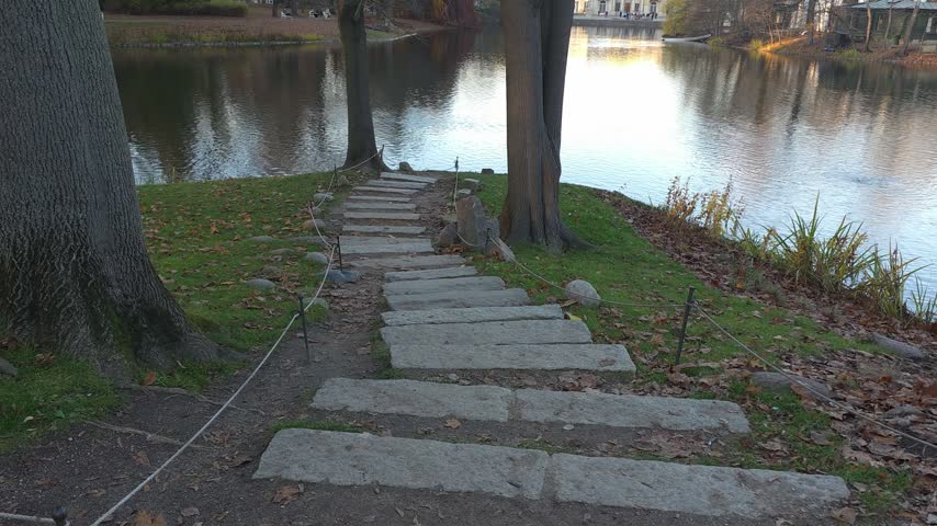 Stone step pathway leading toward a calm lake surrounded by autumn trees. POV shot.