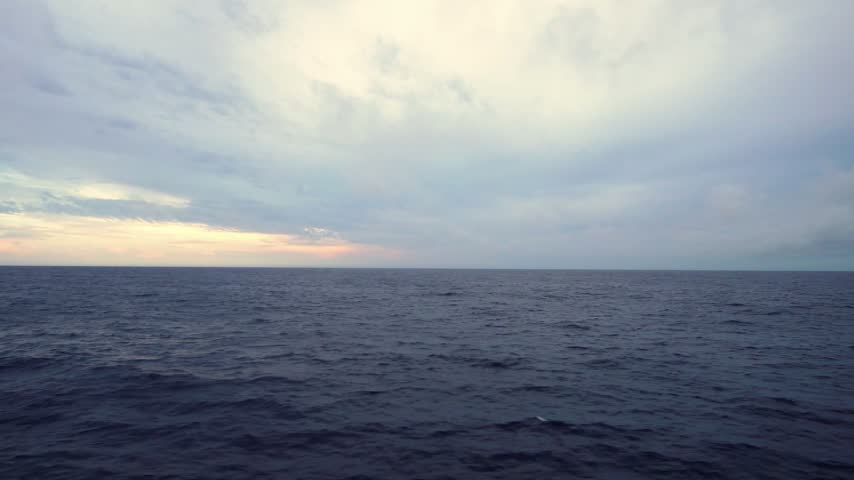 Distant horizon and ocean waves with occasional sea spray from a passenger ship at dusk