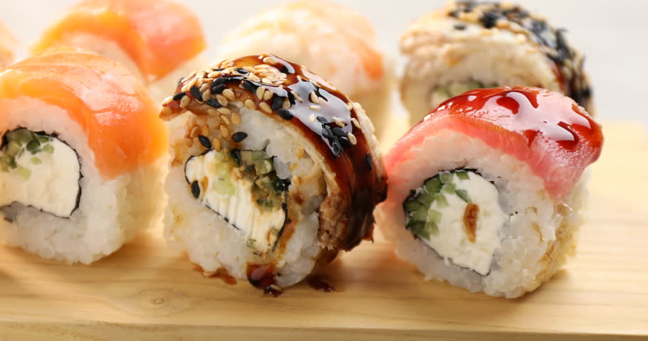 Taking sushi roll with chopsticks from wooden tray, closeup