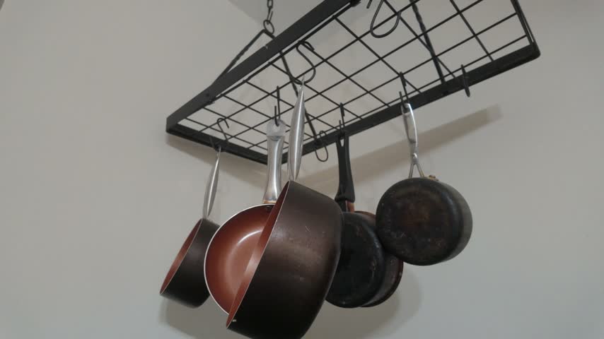 Black metal ceiling pot rack hanging in residential kitchen with various nonstick copper pans and cooking skillets neatly displayed for functional storage solution interior design.