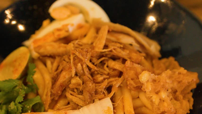Close-up slow pan over traditional Burmese chicken noodle salad served with egg and crispy fritters.