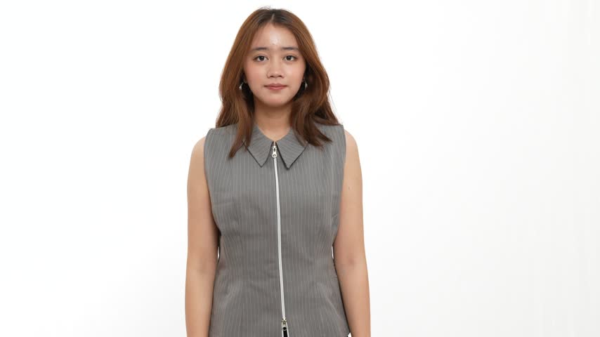 Young woman in a grey sleeveless top placing a finger on her lips to signal silence or secrecy