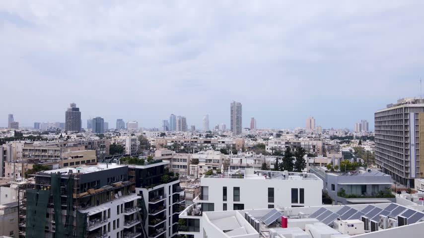 High angle panoramic drone footage showcases dense urban sprawl of Tel Aviv city skyline with modern residential buildings and high rise skyscrapers under moody cloudy weather.