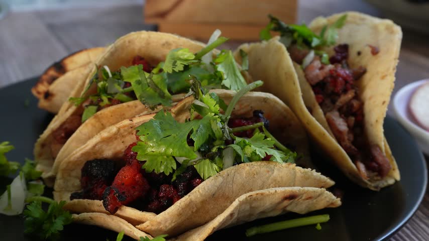 Tacos with fresh cilantro and lime, arranged on a dark plate. Ideal for restaurant advertisements, food blogs, or cultural events.