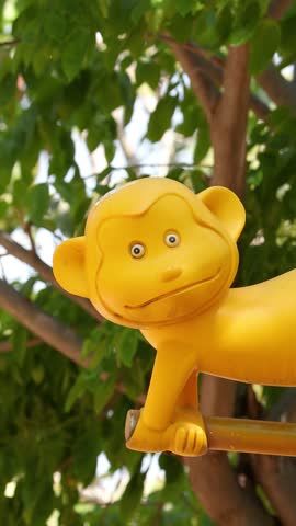 A yellow monkey statue sits on playground bars against green trees in Lumpini Park, Bangkok.