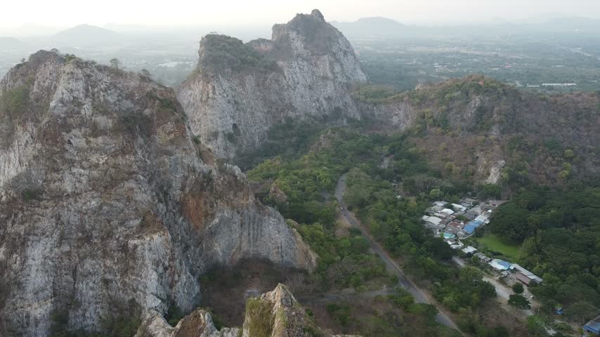 Aerial pan from rugged limestone peaks toward a town and patchwork farmland.