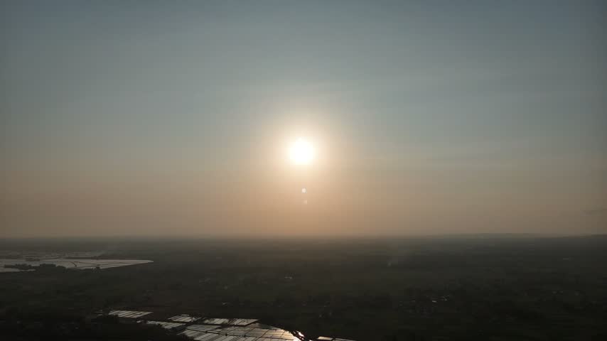 Aerial view of bright glowing sun over hazy rural landscape and reflecting ponds during sunset