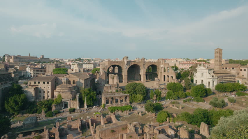 Elevated view across the Roman Forum in Rome, showing ancient ruins, Basilica of Maxentius, trees, and surrounding city.
