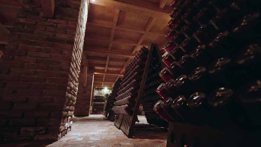 Triangular wooden riddling racks packed with bottles stand beside an old wine press in a warm lit Georgian cellar.