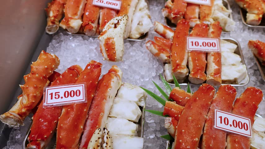 High angle close up footage showing assortment of raw king crab legs organized on trays over bed of ice at fish market stall ready for purchase.