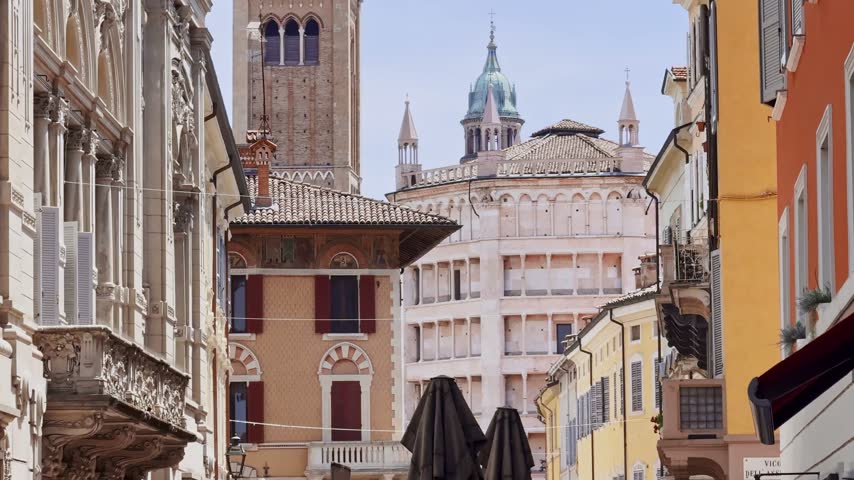 Telephoto view through central Parma toward the Cathedral bell tower and Baptistery, framed by colorful historic facades and layered medieval rooftops.