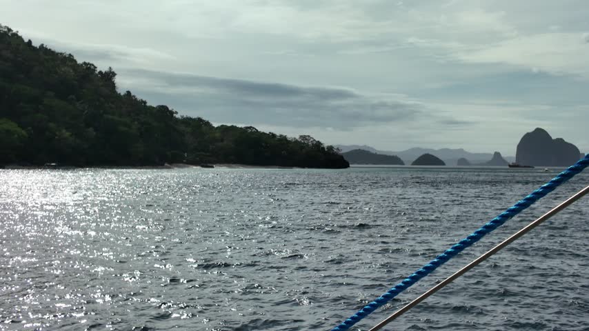 Blue boat ropes frame shimmering sea and distant limestone islets under cloudy sky in El Nido, Philippines