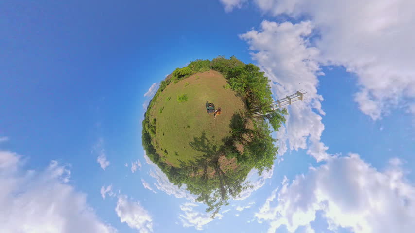 Little Planet View of Two Tourists Walking Across Open Grassy Hill Near Observation Tower, Surrounded by Blue Sky and Tropical Vegetation, Travel and Freedom.
