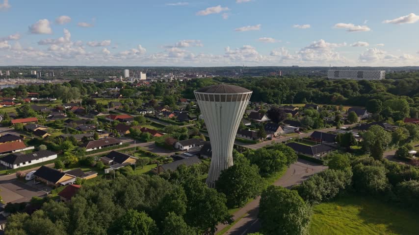 Drone orbit around the historic mushroom-shaped water tower on Sjaellandsvej, revealing the cityscape of Kolding, surrounding greenery, and the scenic urban landscape of southern Denmark.