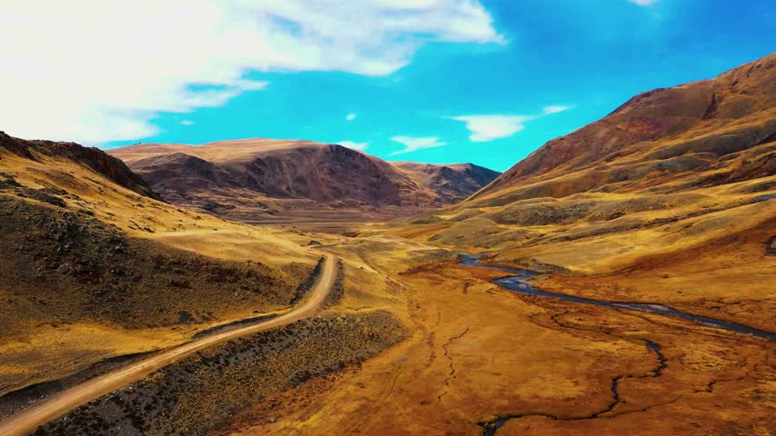 Golden-hued terrain flanks a rugged rural highway beneath a bright blue sky.
