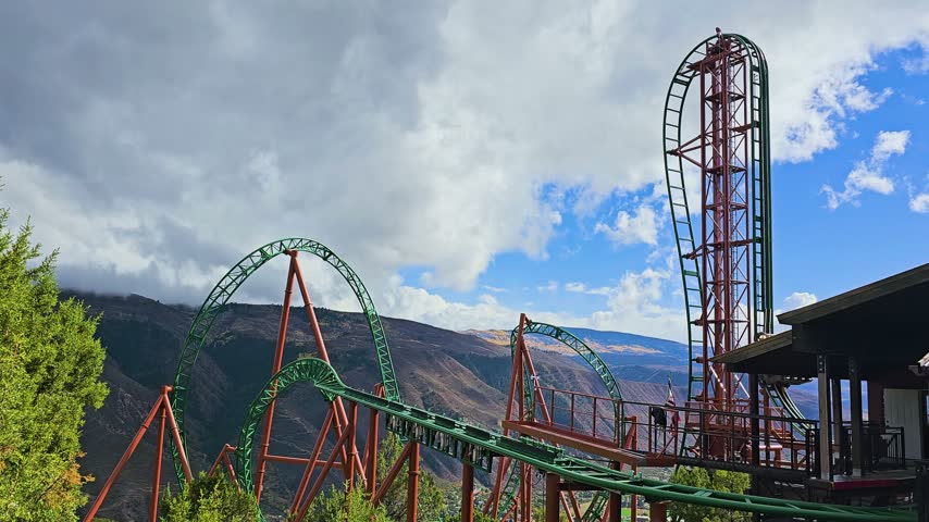 Scenic amusement park roller coaster rises above Glenwood Springs, Colorado, with multiple loops, twisting track, rugged mountain ridges, autumn foliage, and dramatic outdoor adventure.