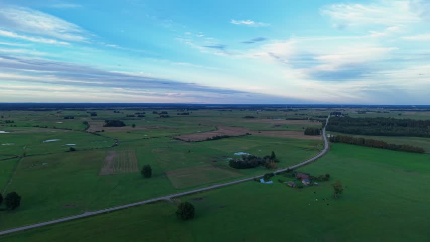 Sweeping aerial footage of open countryside at dusk, featuring winding rural roads, scattered farms, lush green fields, and dramatic cloud-streaked skies in tranquil natural light.