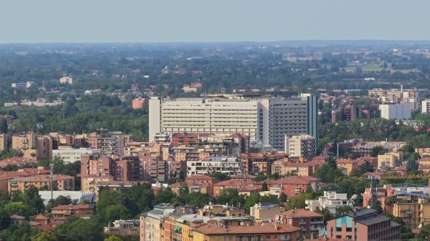 Bologna cityscape featuring the large modern Ospedale Maggiore hospital building towering over residential buildings and a green urban landscape under a clear sky in Italy