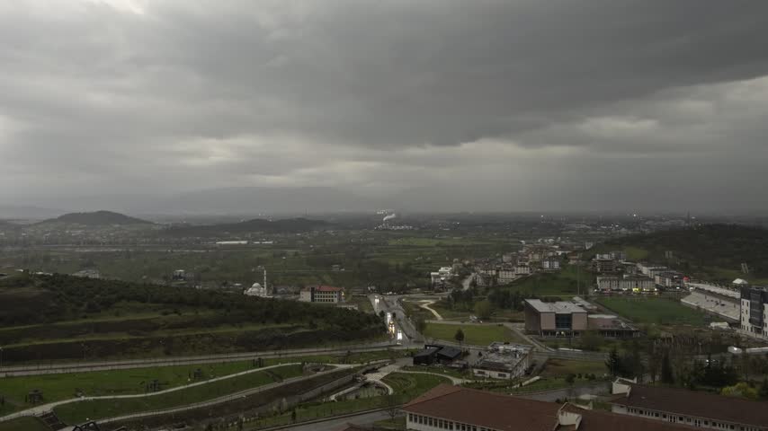 Wide view of a small town and green countryside beneath heavy dark storm clouds approaching