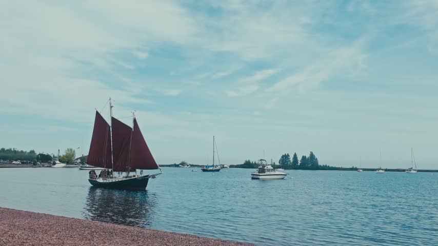 The Harbor of Grand Marais as a vintage sailing ship passes by the beach on a bright summer day.