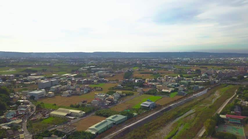 Drone panorama of railway tracks running through a suburban landscape with fields, homes and scattered development in Taiwan, 4K.