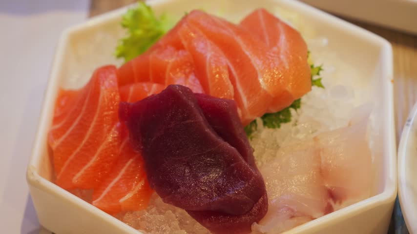 Sashimi platter of fresh salmon, tuna and white fish slices served on ice in a white bowl, a traditional Japanese dish.